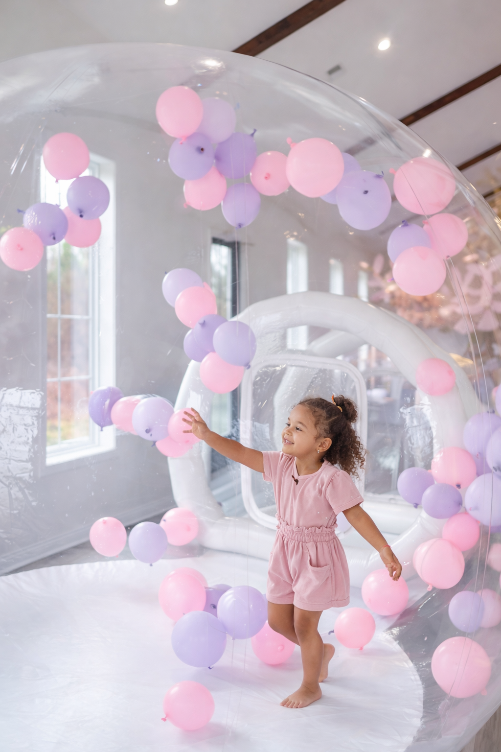 Child playing inside luxury bubble house with pink and purple balloons