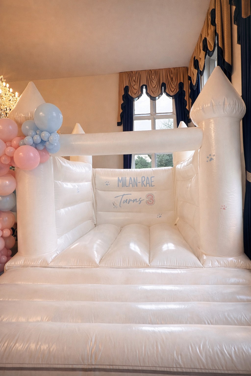White bouncy castle set up in a luxury venue with pink and blue balloon garland