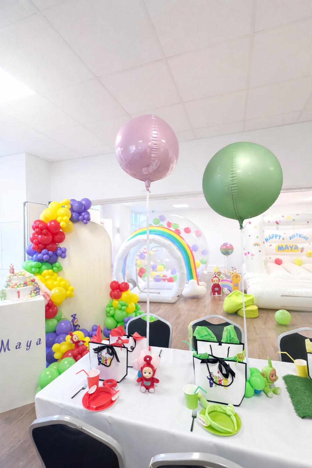 Full Teletubbies themed birthday party setup with bouncy castle and balloon arch