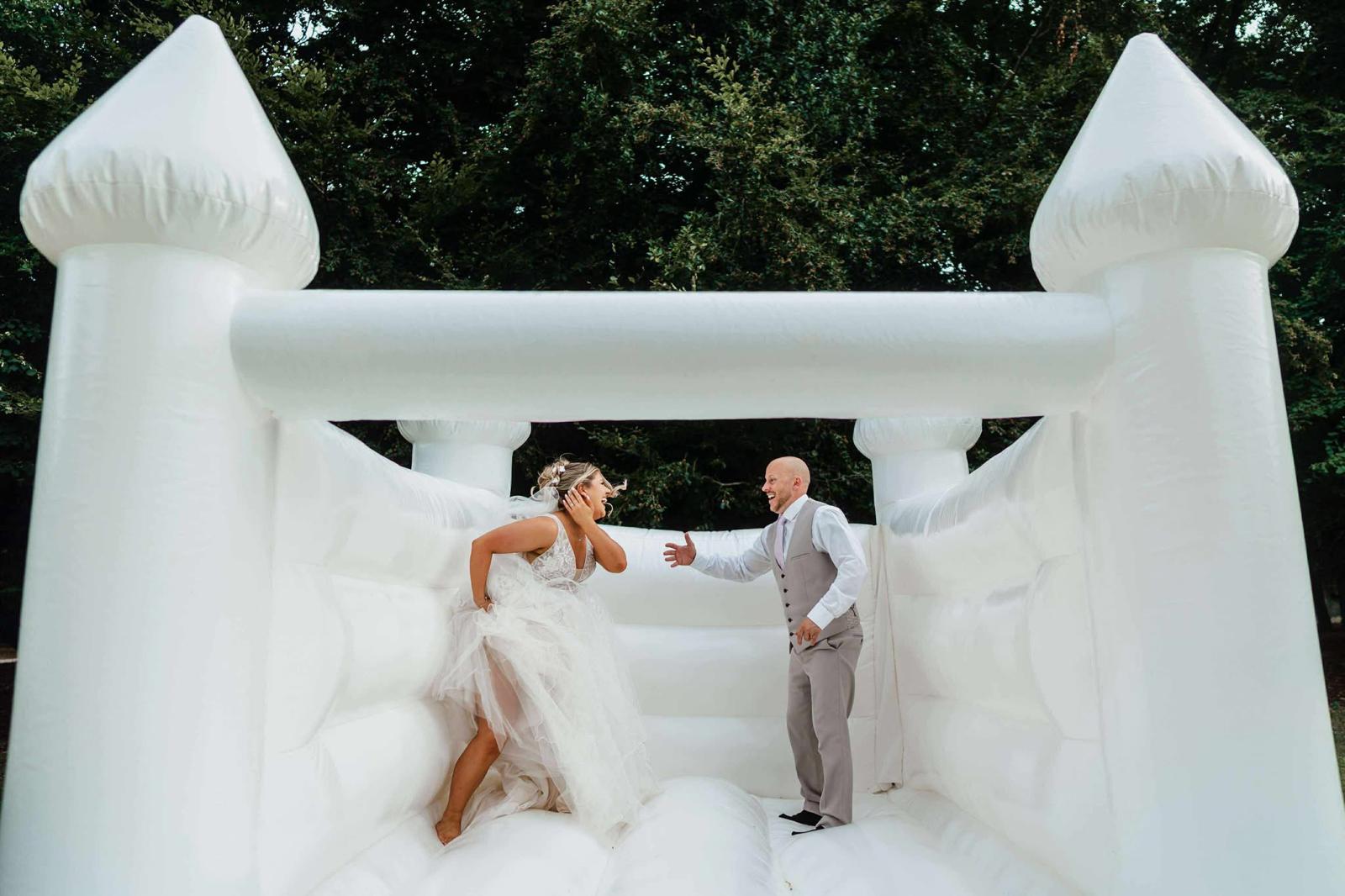 Bride and groom laughing together on a white bouncy castle at their wedding